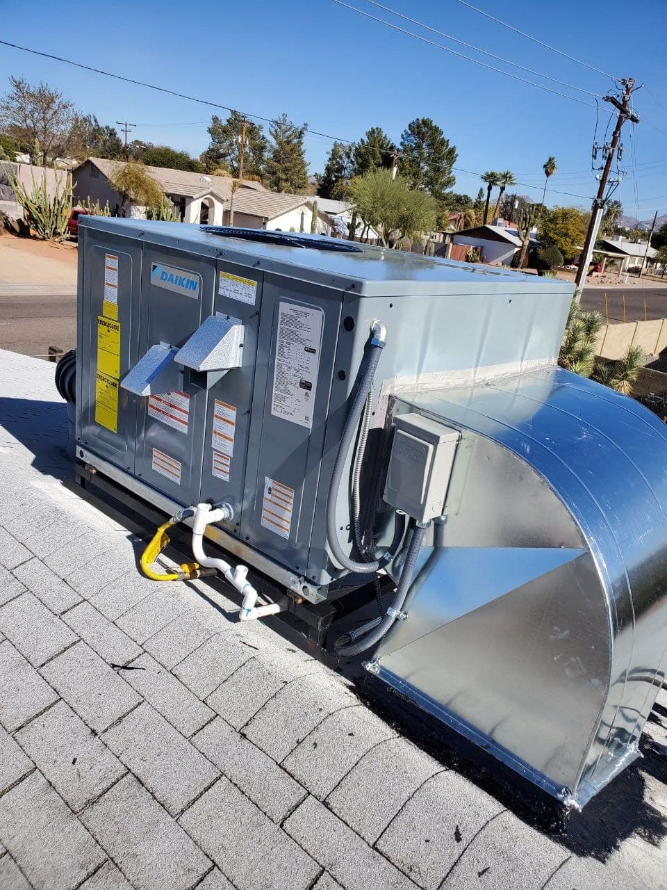 A newly installed Daikin rooftop package unit joined to new sheet-metal ductwork on a shingle roof