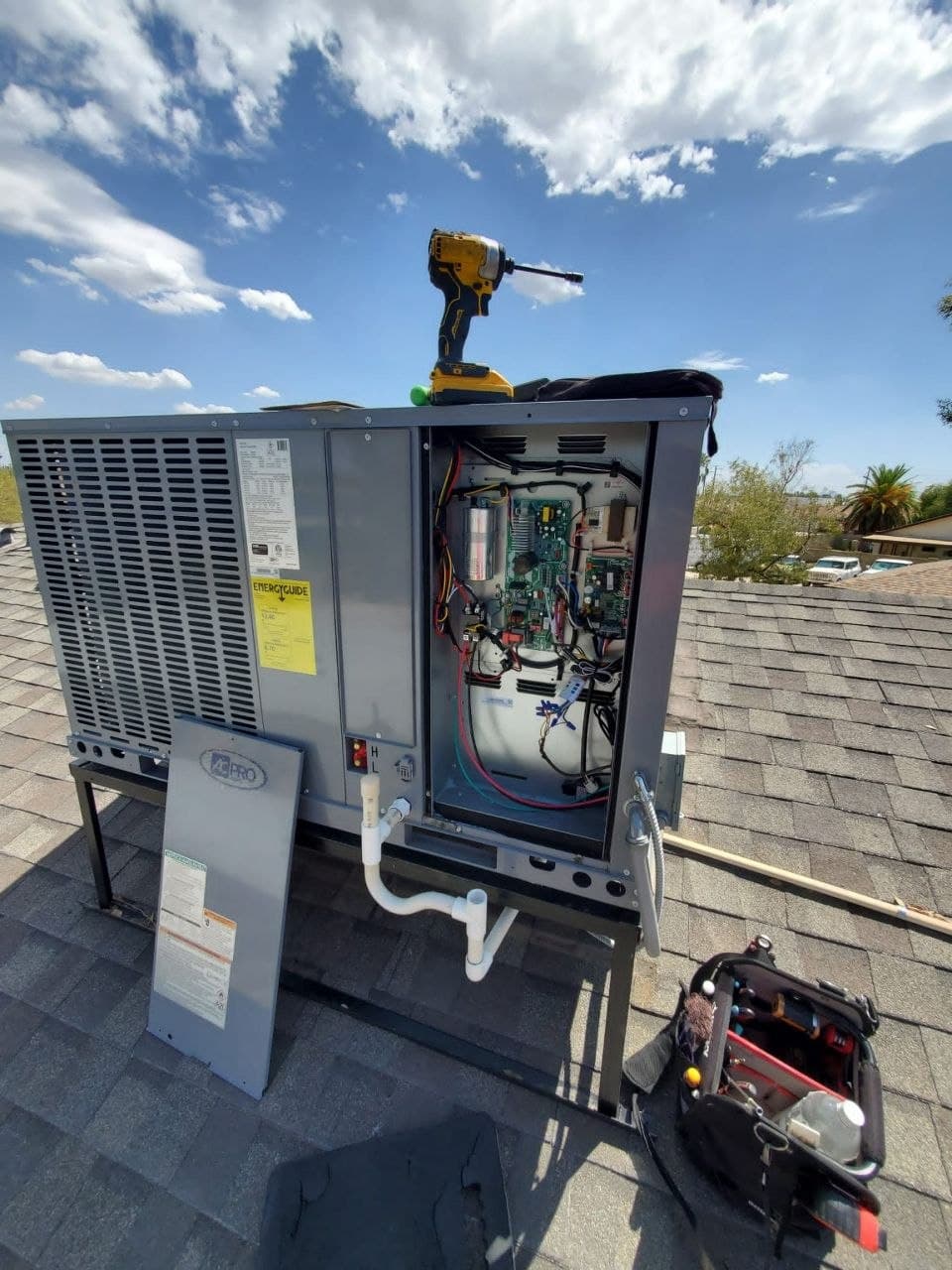 The control compartment of a rooftop package unit opened for service, with an impact driver and tool bag on the roof