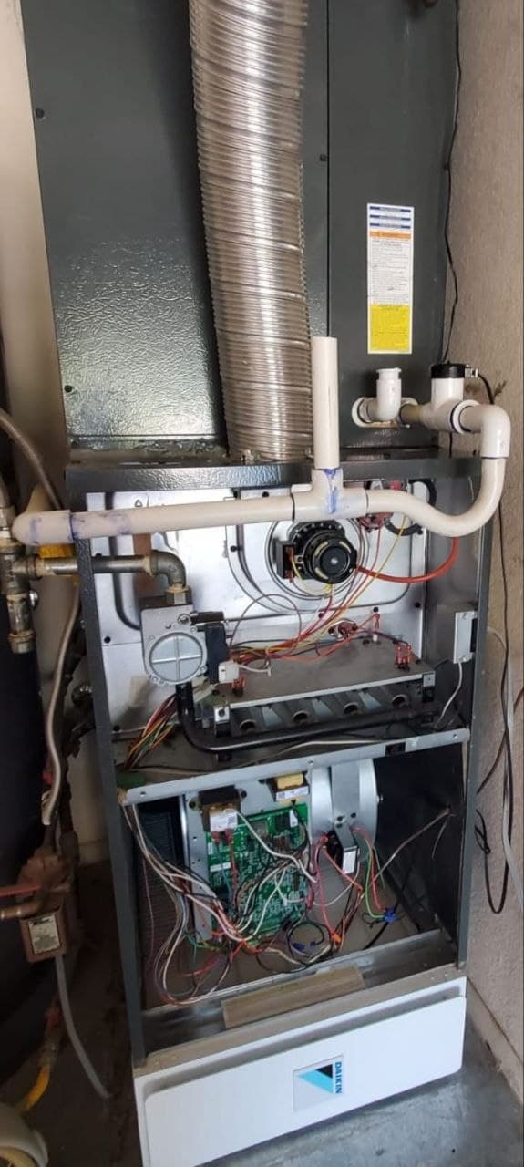 A Daikin furnace with both access panels off, exposing the burner assembly, inducer and control board