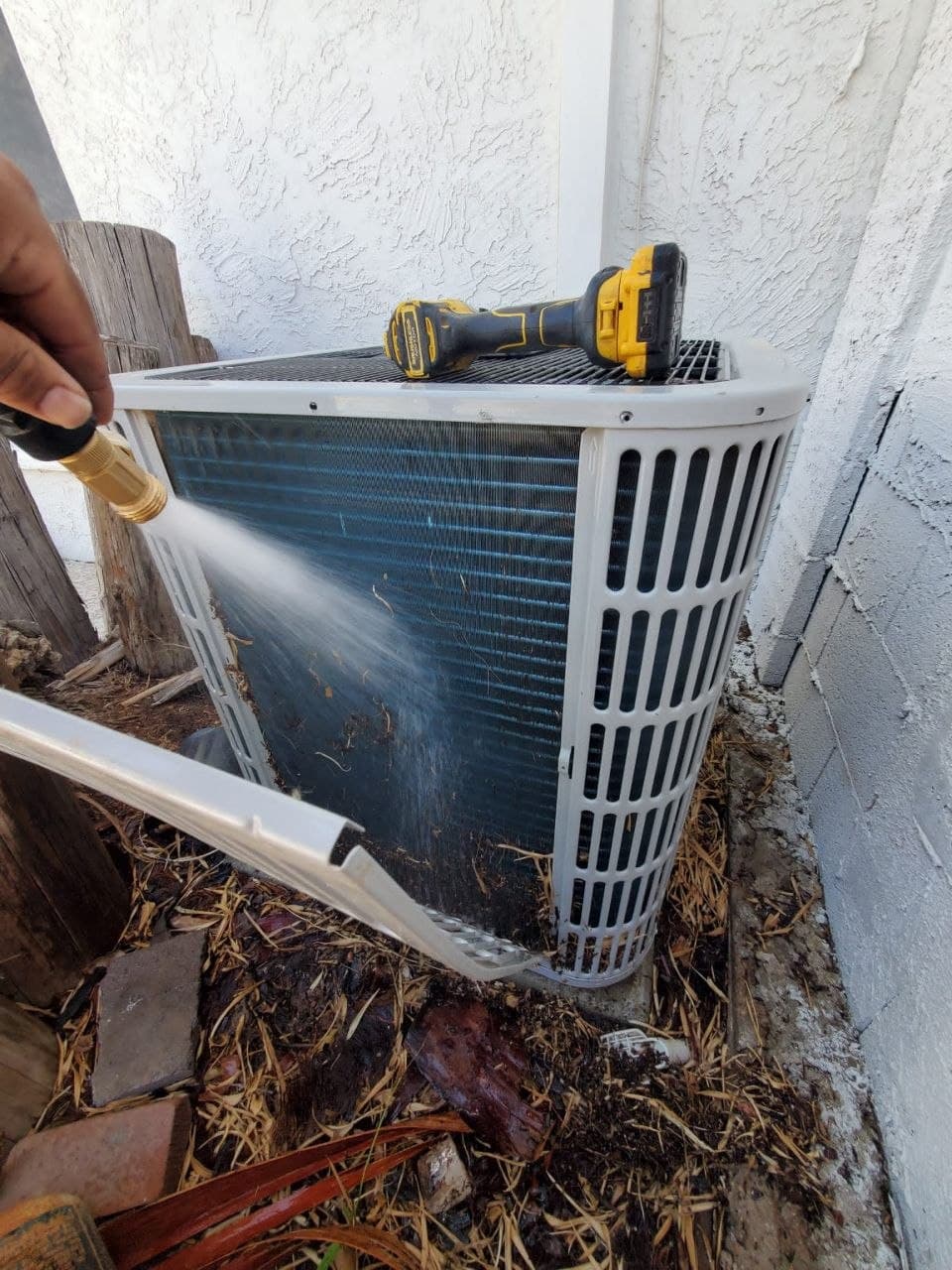 Rinsing dust and debris out of a residential condenser coil with a hose during a tune-up